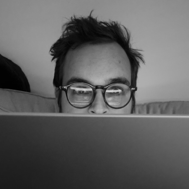 A wide-eyed human head peering at you from behind a laptop screen with wild hair.